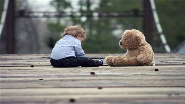 Boy sitting on wooden bridge with  teddy bear